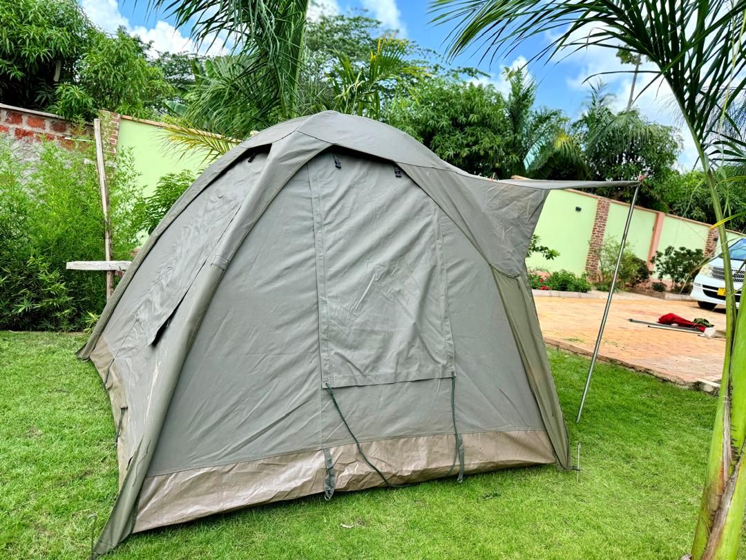 Una carpa montada sobre un césped con un muro de ladrillo y vegetación al fondo.