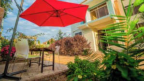 A patio area with a red umbrella, a white chair, and a table. - Kilimanjaro Home Of Travelers (Moshi)