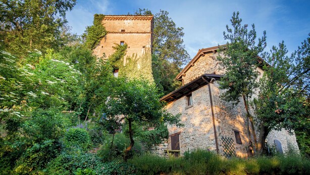 A stone building with a tower, surrounded by lush greenery. - 1500 Fortified house in Borgo Fontanini (Emilia-Romagna)