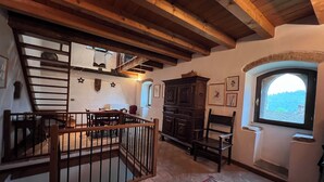 A rustic interior with exposed wooden beams, a staircase, a dining area, and a view through a window. - 1500 Fortified house in Borgo Fontanini (Emilia-Romagna)