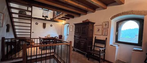 Un interior rústico con vigas de madera a la vista, una escalera, una zona de comedor y vistas por una ventana.