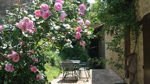 A patio with a table and chairs, surrounded by lush pink roses and greenery. - 1500 Fortified house in Borgo Fontanini (Emilia-Romagna)