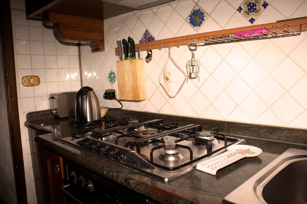 A kitchen with a gas stove, a toaster, and a hanging utensil rack. - 1500 Fortified house in Borgo Fontanini (Emilia-Romagna)