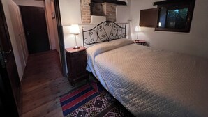 A bedroom with a bed, two bedside tables with lamps, a wooden floor, a patterned rug, and a window. - 1500 Fortified house in Borgo Fontanini (Emilia-Romagna)
