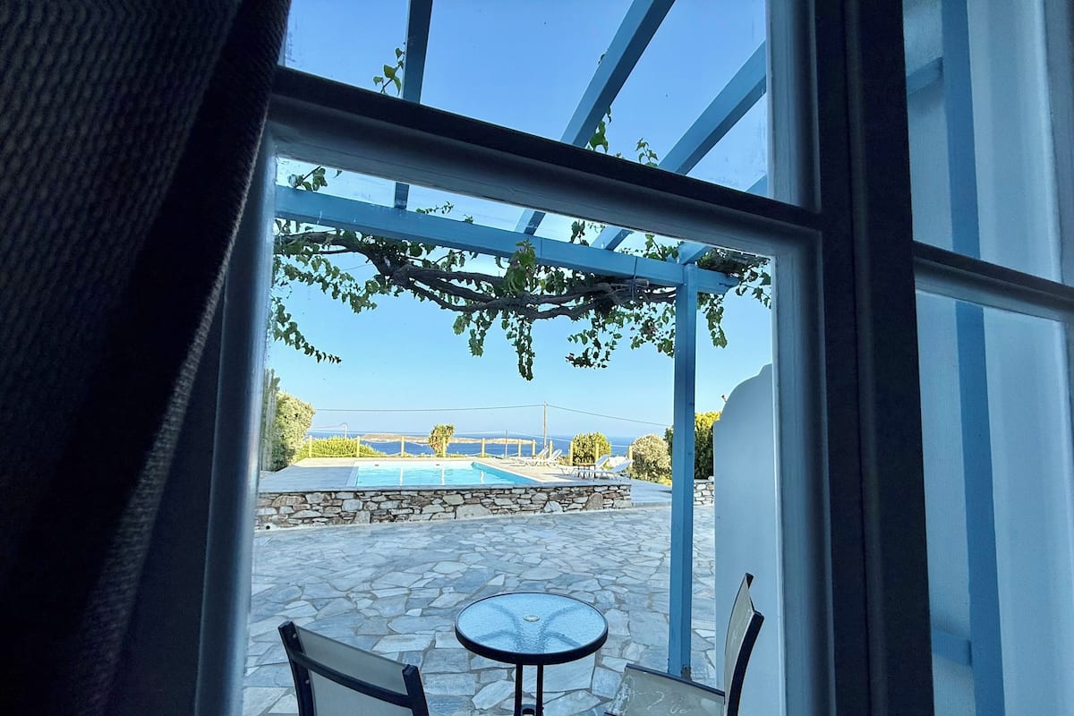 A view from a window to an outdoor patio with a stone floor, two chairs, and a small table.