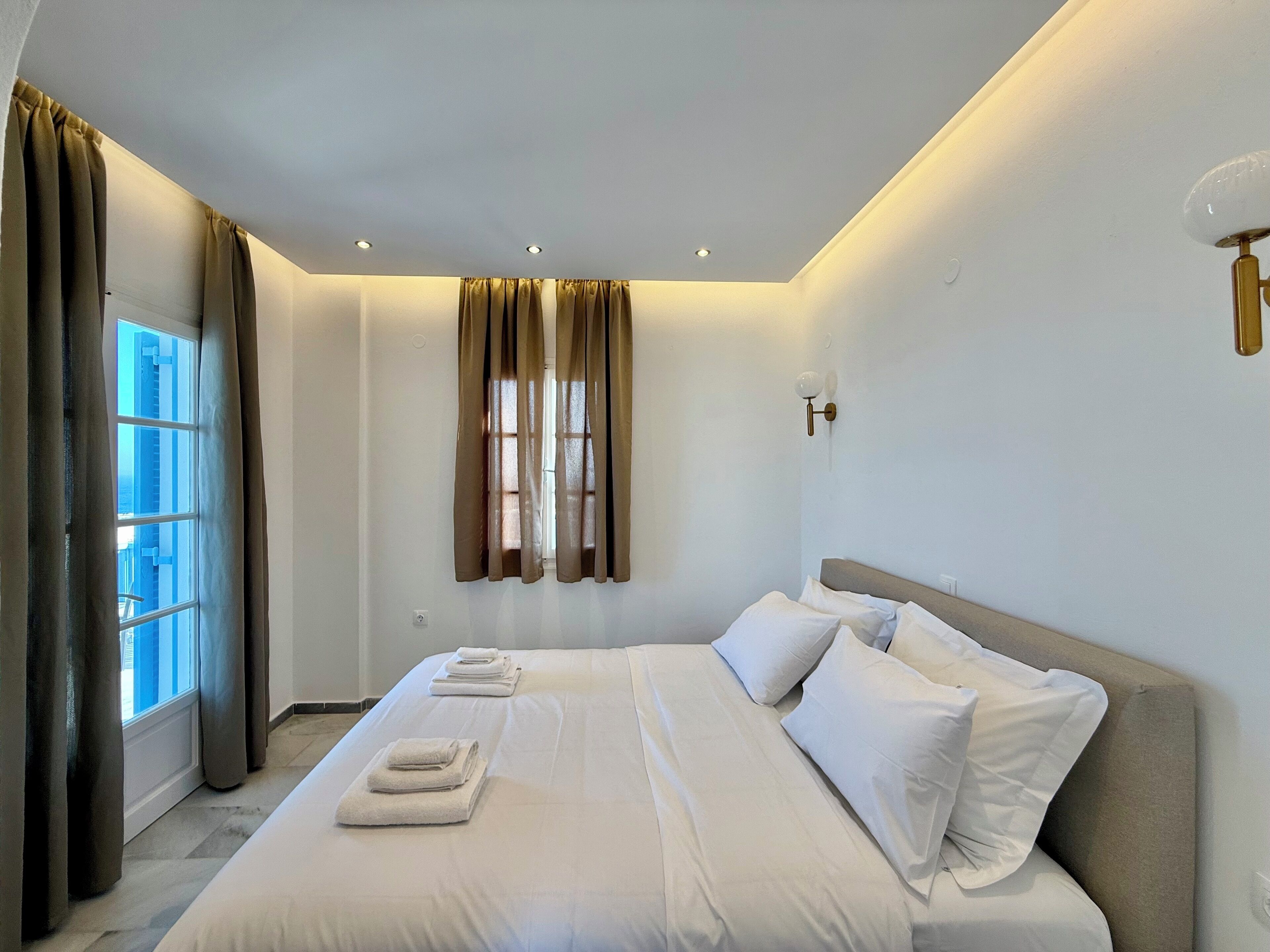 Una camera d'albergo con un letto grande, una finestra con tende e un lampadario a parete.