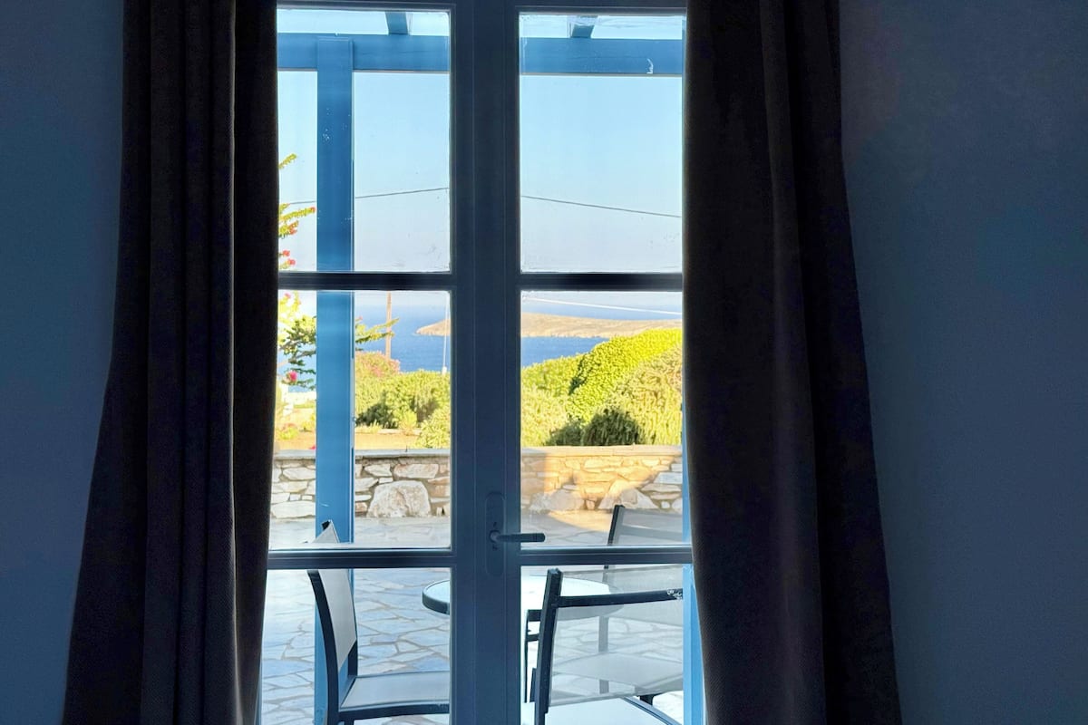 A room with a large window, a view of the sea, and a stone wall.