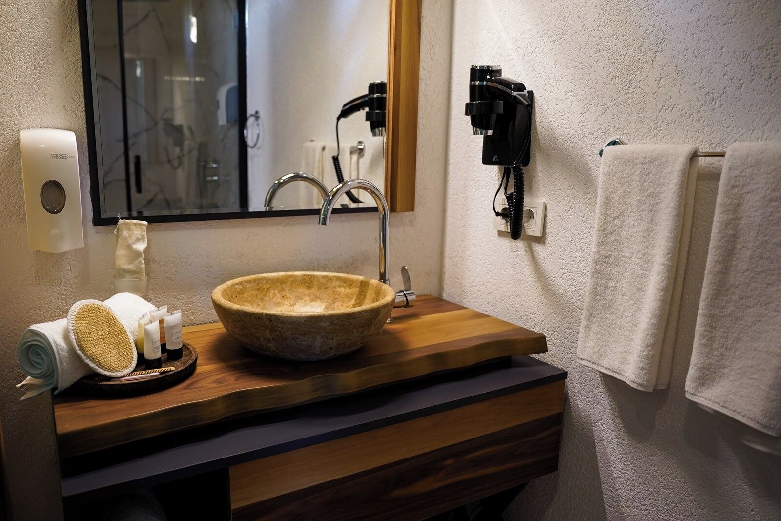 A bathroom with a wooden vanity, a stone basin, a towel rack, and a hand soap dispenser.