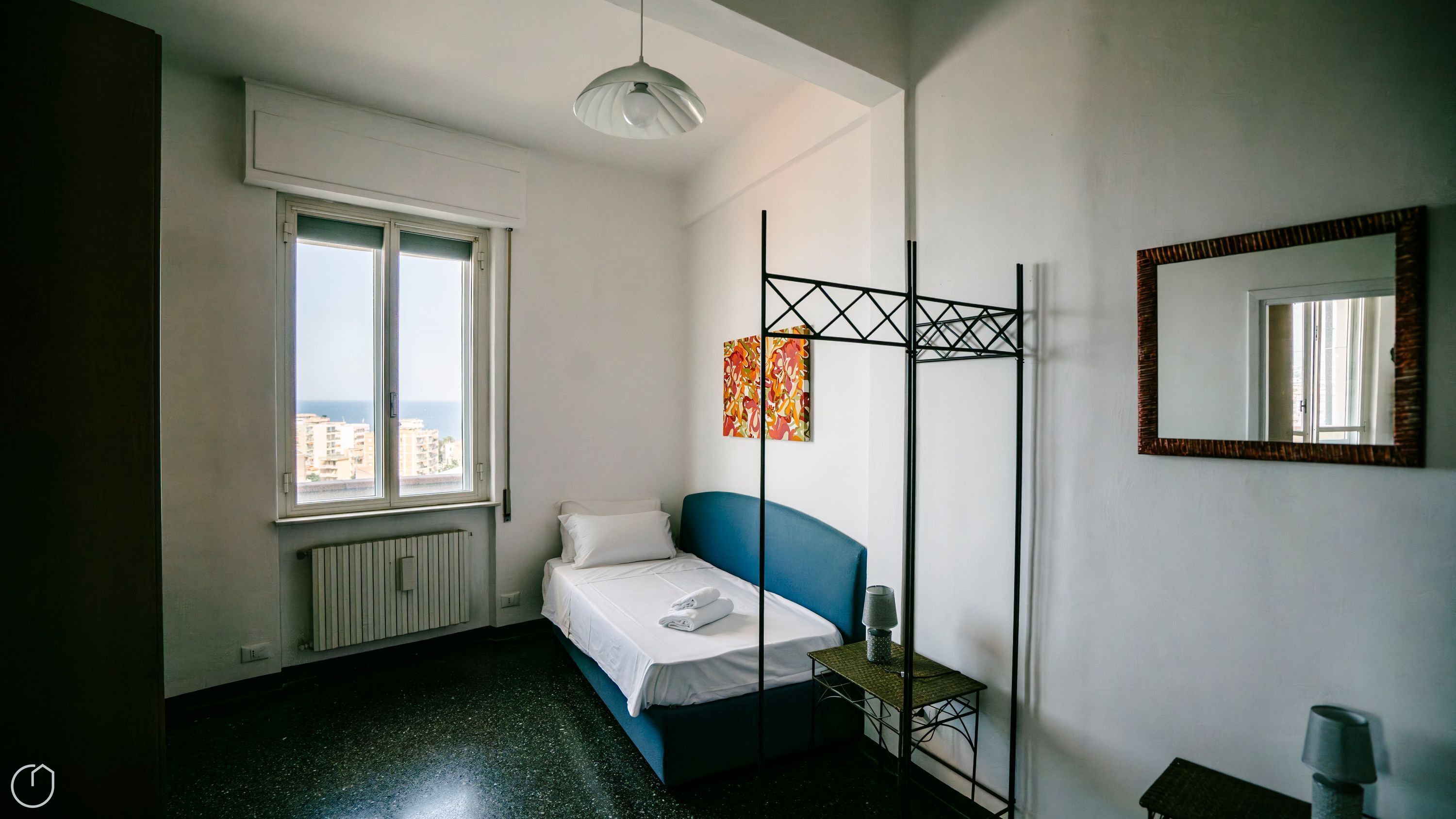 Ein Schlafzimmer mit Bett, Heizkörper, Fenster mit Blick und Stehlampe sowie einem Spiegel.