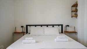 En pænt redt seng med hvide sengetæpper og to håndklæder, en sort sengegavl samt natborde med lamper.