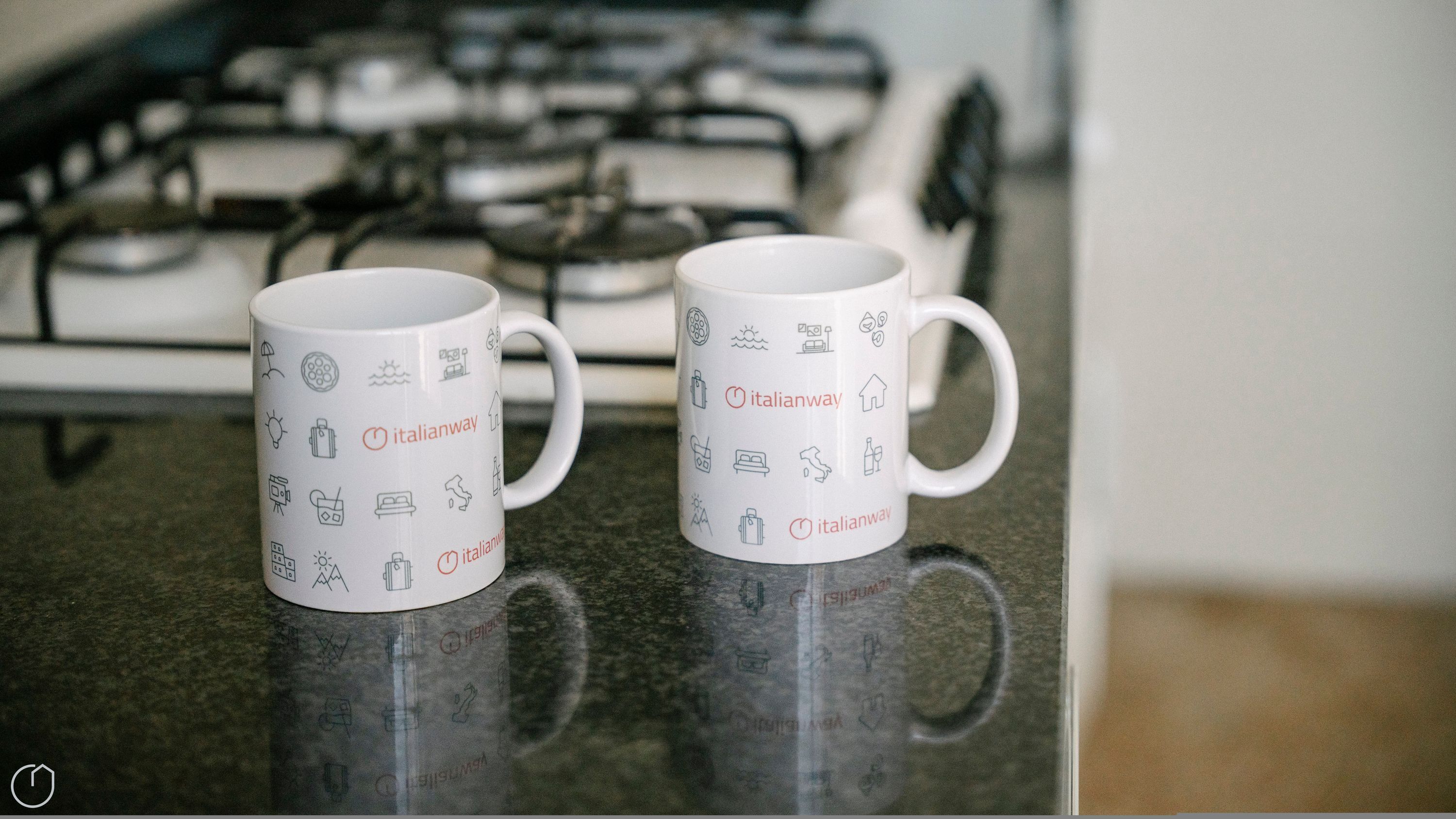 Two white mugs with Italian-themed icons on a kitchen counter.