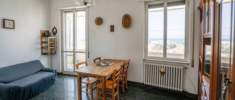 Una habitación con una mesa de comedor de madera, sillas, un sofá azul y una ventana con vistas a edificios.