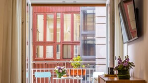A room with a wooden floor, a wooden cabinet, a table with chairs, a potted plant, and a view through a door to an outdoor balcony with a railing. - Direlo Guest House (Naples)