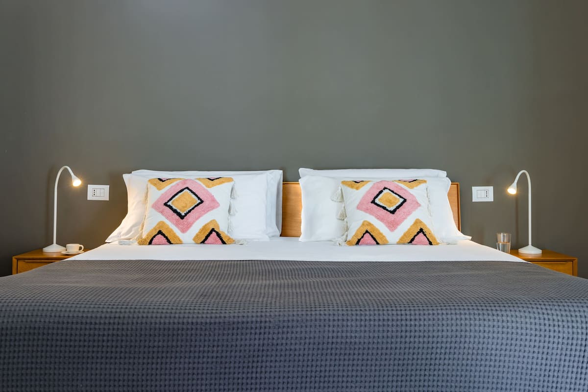 A neatly made bed with patterned pillows, two bedside lamps, and a bedside table with a cup and glass.