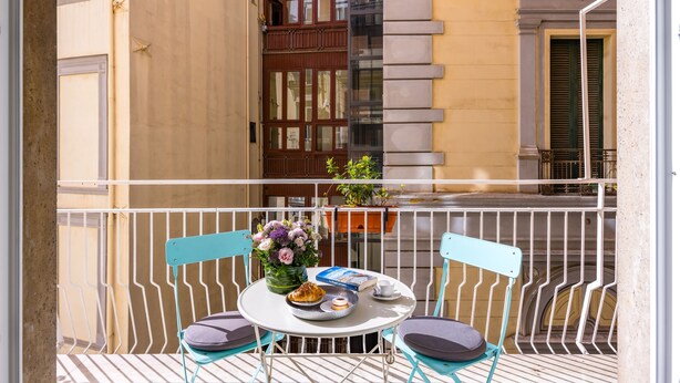 A balcony with a table set for two, featuring a book, a plate with a pastry, and a vase with flowers. - Direlo Guest House (Naples)