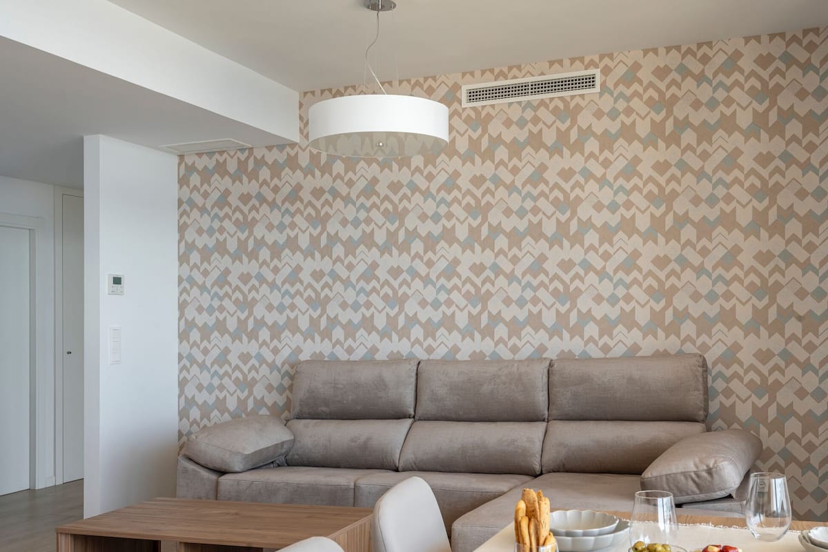 Uma sala de estar moderna com um sofá cinzento, mesa de centro de madeira e um espaço de jantar com toalha branca e comida.