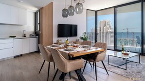 A modern kitchen with white cabinets, a flat-screen TV, and a dining area with a wooden table and chairs. - Torre Sakura (Benidorm)