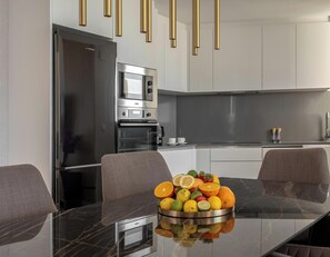 Una cocina moderna con un refrigerador de acero inoxidable, horno empotrado y microondas. Hay una mesa de comedor con un frutero en el centro.