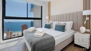 A modern bedroom with a large window, a bed with neatly folded towels, and a nightstand with a lamp. - Torre Sakura (Benidorm)