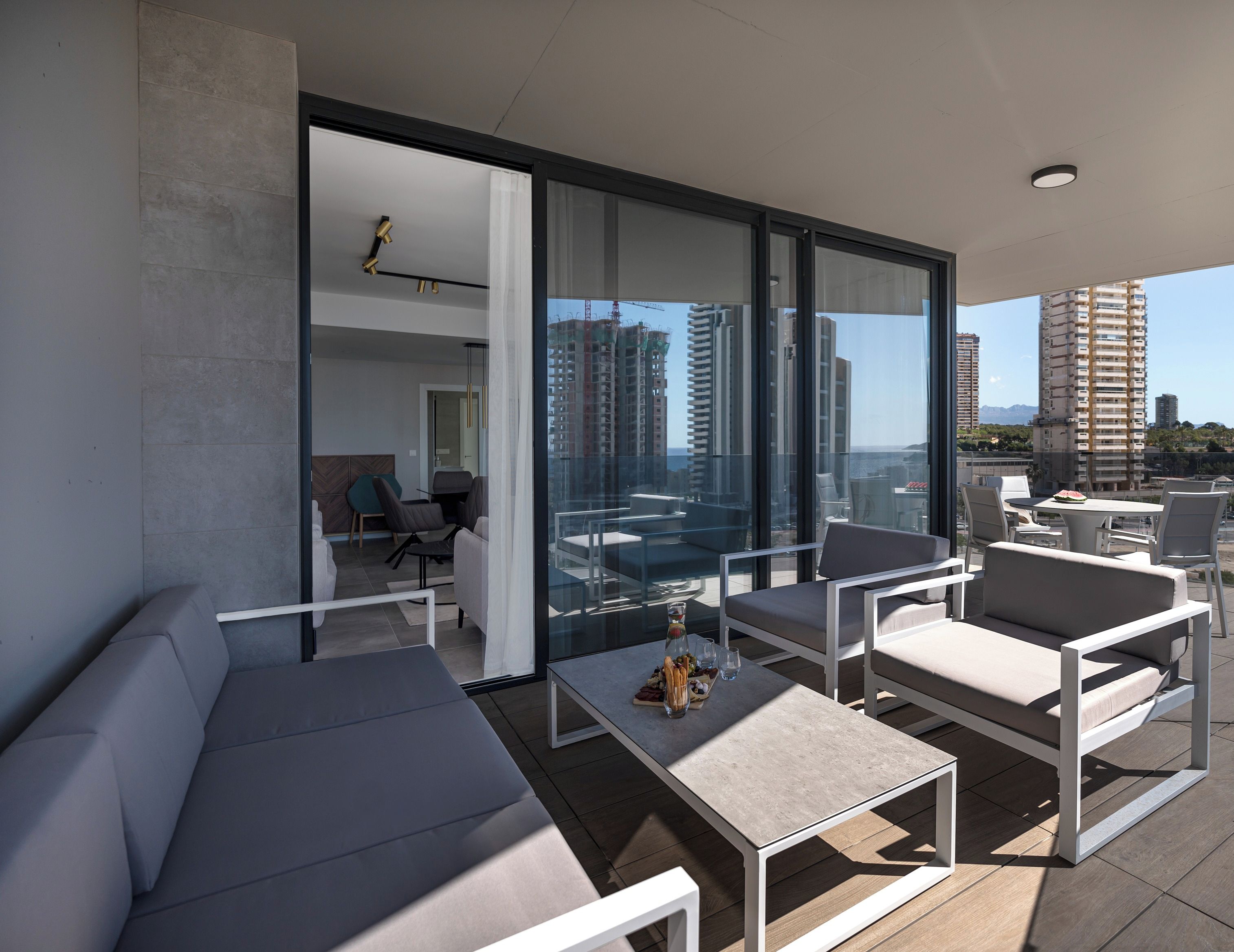 Un balcón moderno con sofá, sillas y una mesa, con vistas a un paisaje urbano con edificios altos.