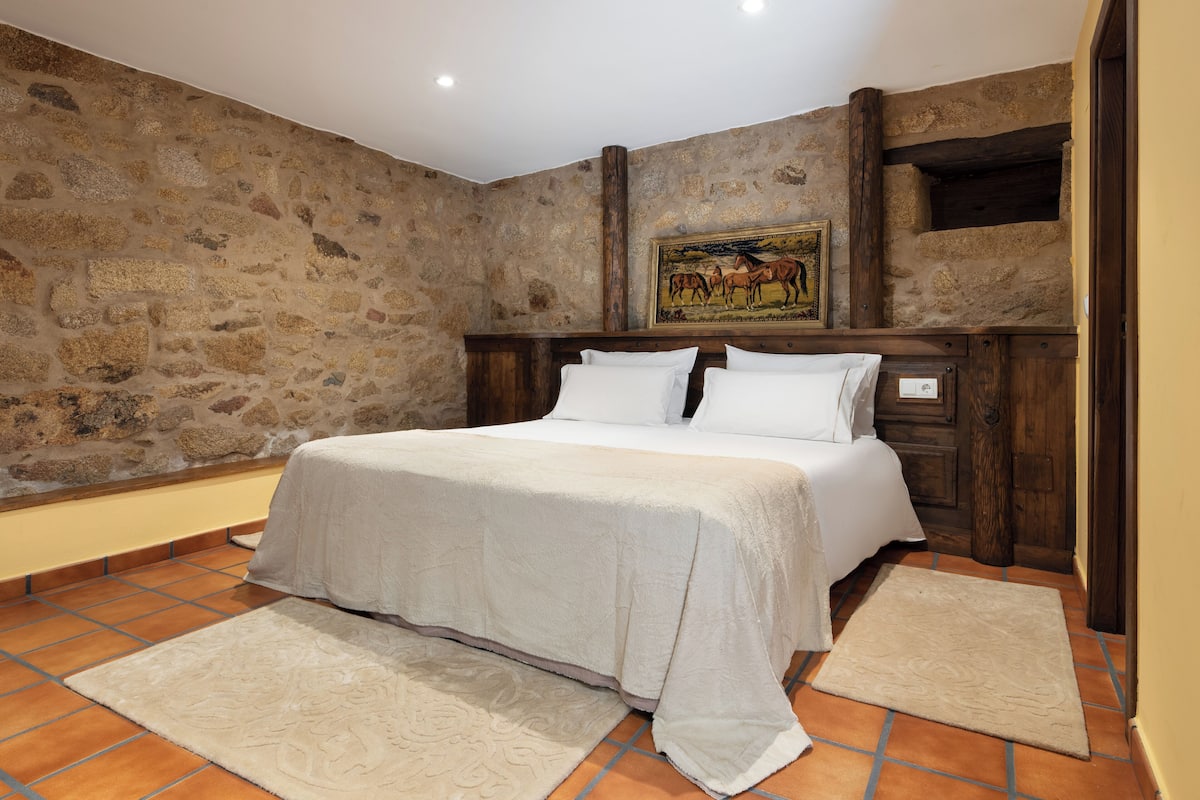 A bedroom with a stone wall, a bed with white bedding, and a painting above the bed.