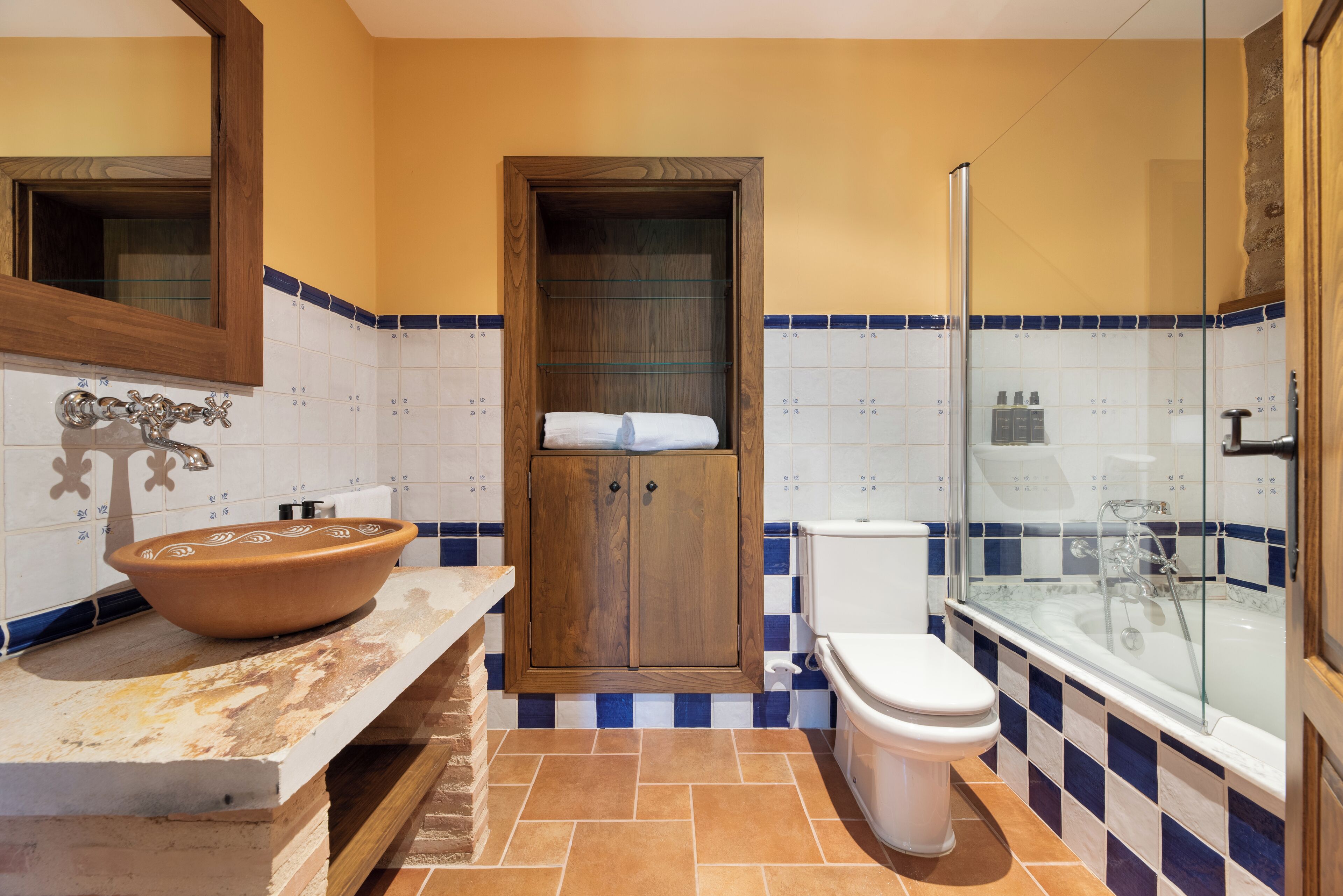 A bathroom with a wooden cabinet, a white toilet, and a glass-enclosed shower.