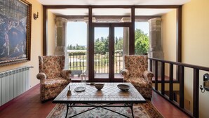 Un balcon agrémenté de deux fauteuils ornés de motifs floraux, d’une table carrelée et offrant une vue sur la verdure à travers des portes vitrées.