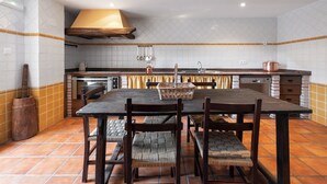 Une cuisine avec un mur recouvert de carreaux, des chaises en bois, une table en bois foncé et une casserole en cuivre posée sur le comptoir.