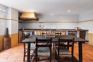 Cozinha com painel de azulejos, cadeiras de madeira, mesa de madeira escura e uma panela de cobre sobre a bancada.