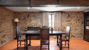 A rustic dining area with a stone wall, wooden table, and antique chairs.