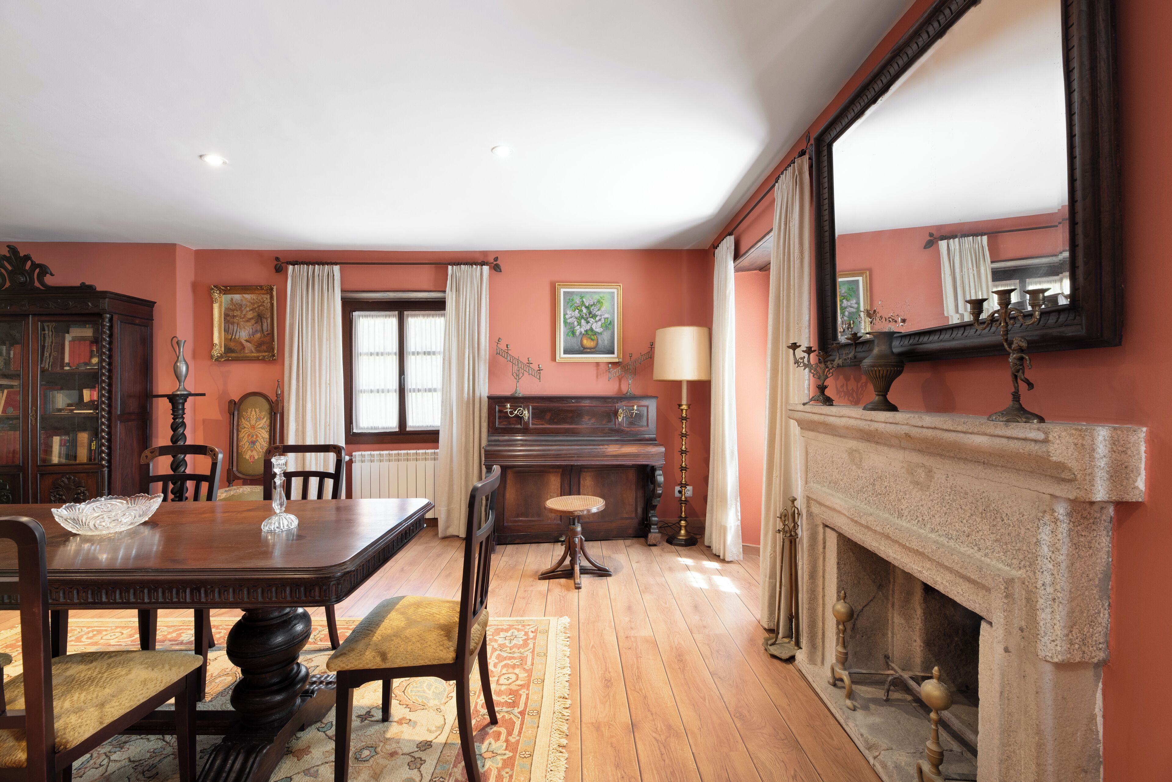 A dining room with a wooden table, chairs, a piano, and a fireplace.