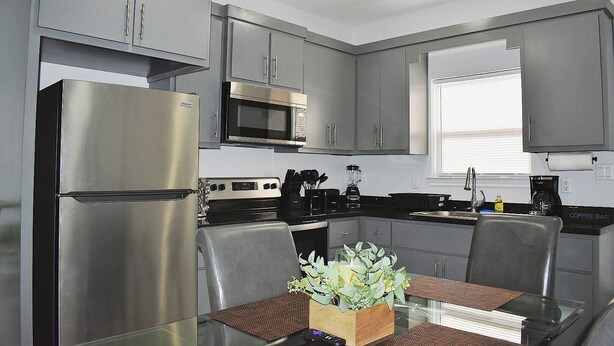 A compact kitchen with stainless steel appliances, grey cabinets, and a dining area with a glass table and chairs.