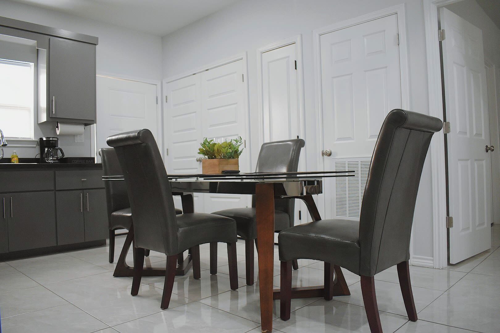 A dining area with a glass-top table, four chairs, and a coffee station.