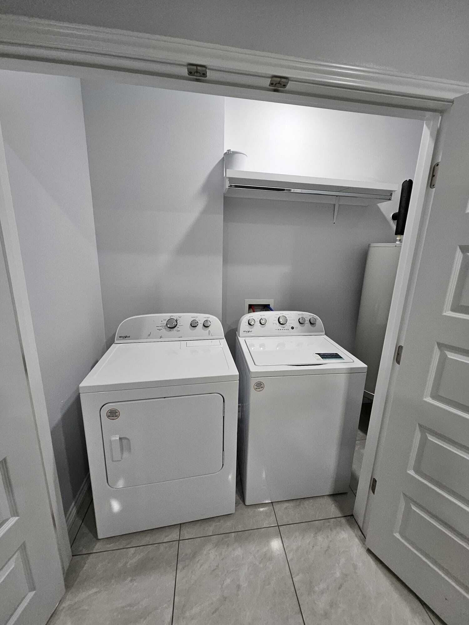 Een wasserette met twee voorladers wasmachines en een droger, witte wanden en een betegelde vloer.