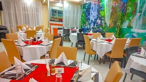 Ein Restaurant mit mehreren gedeckten Tischen, das ein Wandbild mit einem Wasserfall zeigt.