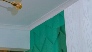 Ein Schlafzimmer mit einem grün strukturierten Kopfende, einem Bett mit weißer Bettwäsche und geometrischen Kissen sowie einem goldenen Ring am Kopfende.