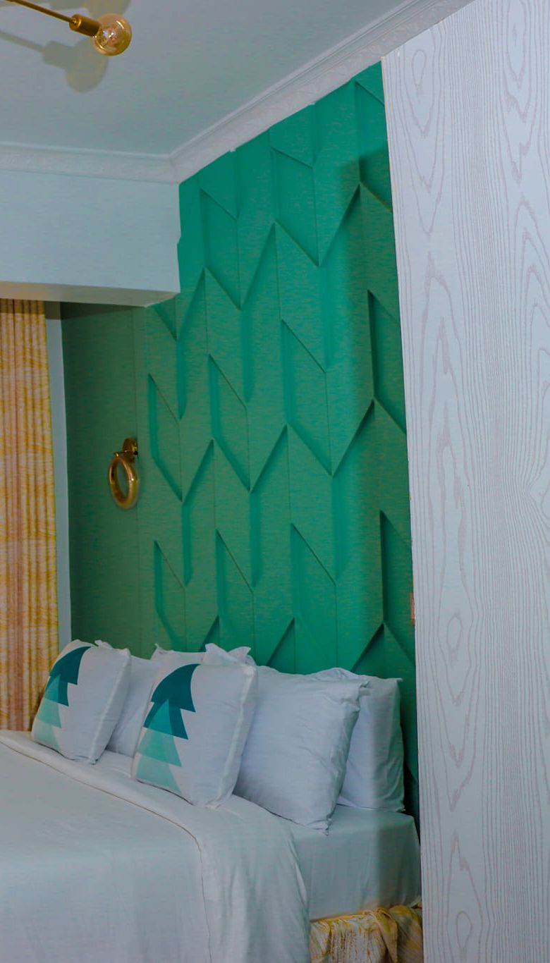 Ein Schlafzimmer mit einem grün strukturierten Kopfende, einem Bett mit weißer Bettwäsche und geometrischen Kissen sowie einem goldenen Ring am Kopfende.