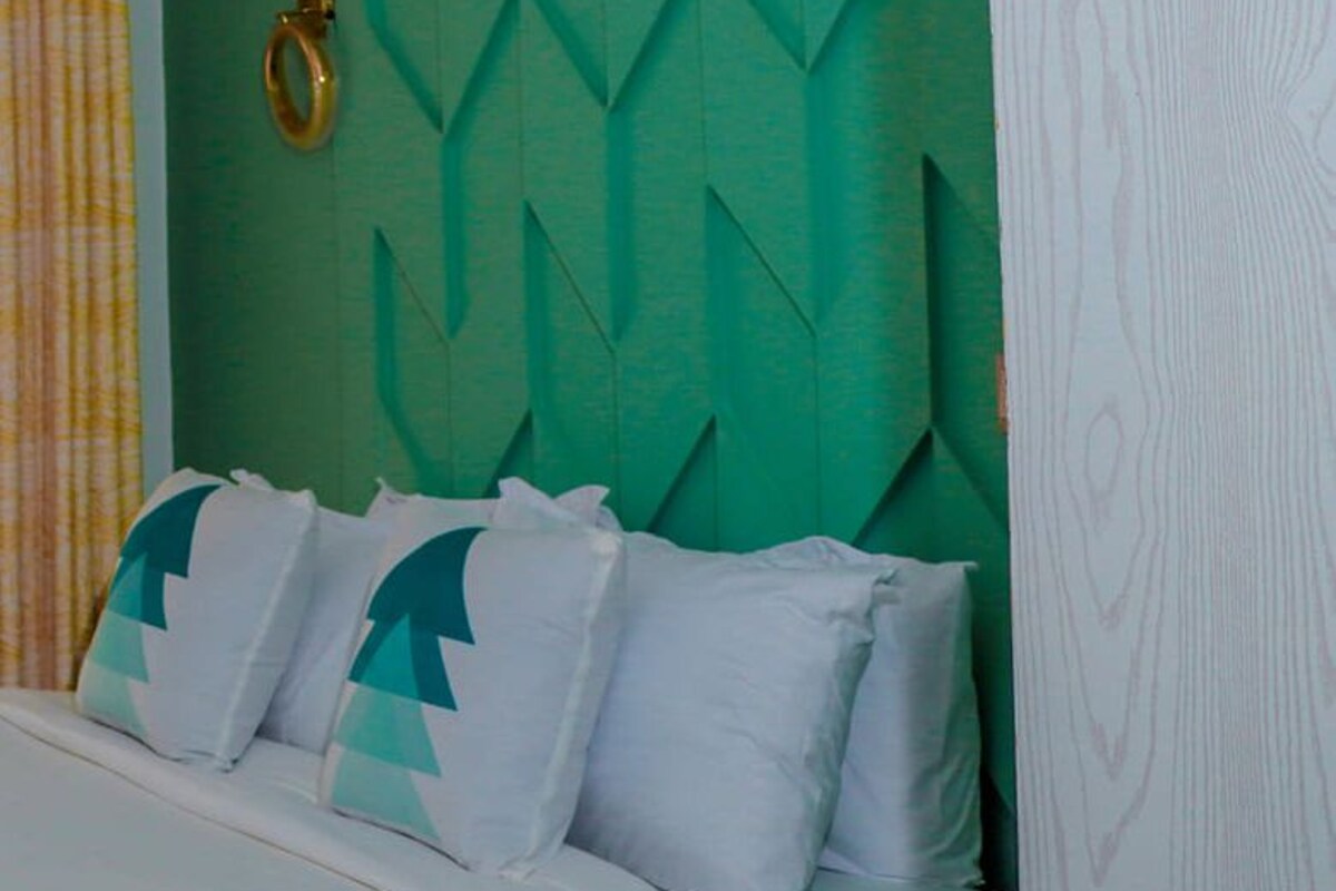 A bedroom with a green textured headboard, a bed with white bedding and geometric pillows, and a gold ring on the headboard.