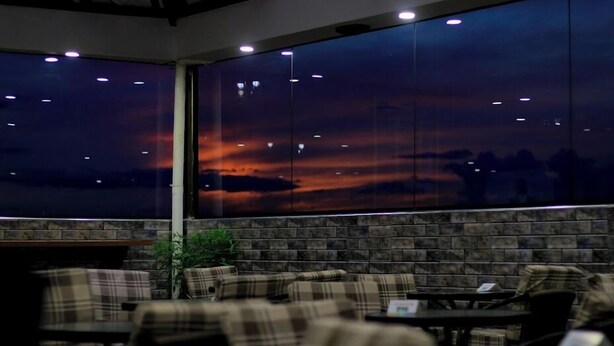 Ein Restaurant mit einem großen Fenster, das einen Sonnenuntergang zeigt, gepolsterten Sitzgelegenheiten und einer Ziegelwand.