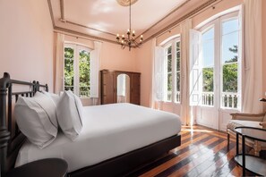 Ein Schlafzimmer mit einem großen Bett, einem Holzkapfenkasten, einem kleinen Tisch und einem Balkon mit Vorhängen.