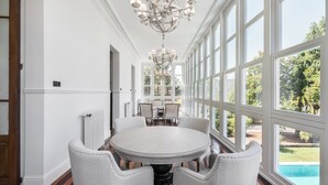 Un coin repas avec une table ronde et six chaises, de grandes fenêtres et un lustre.
