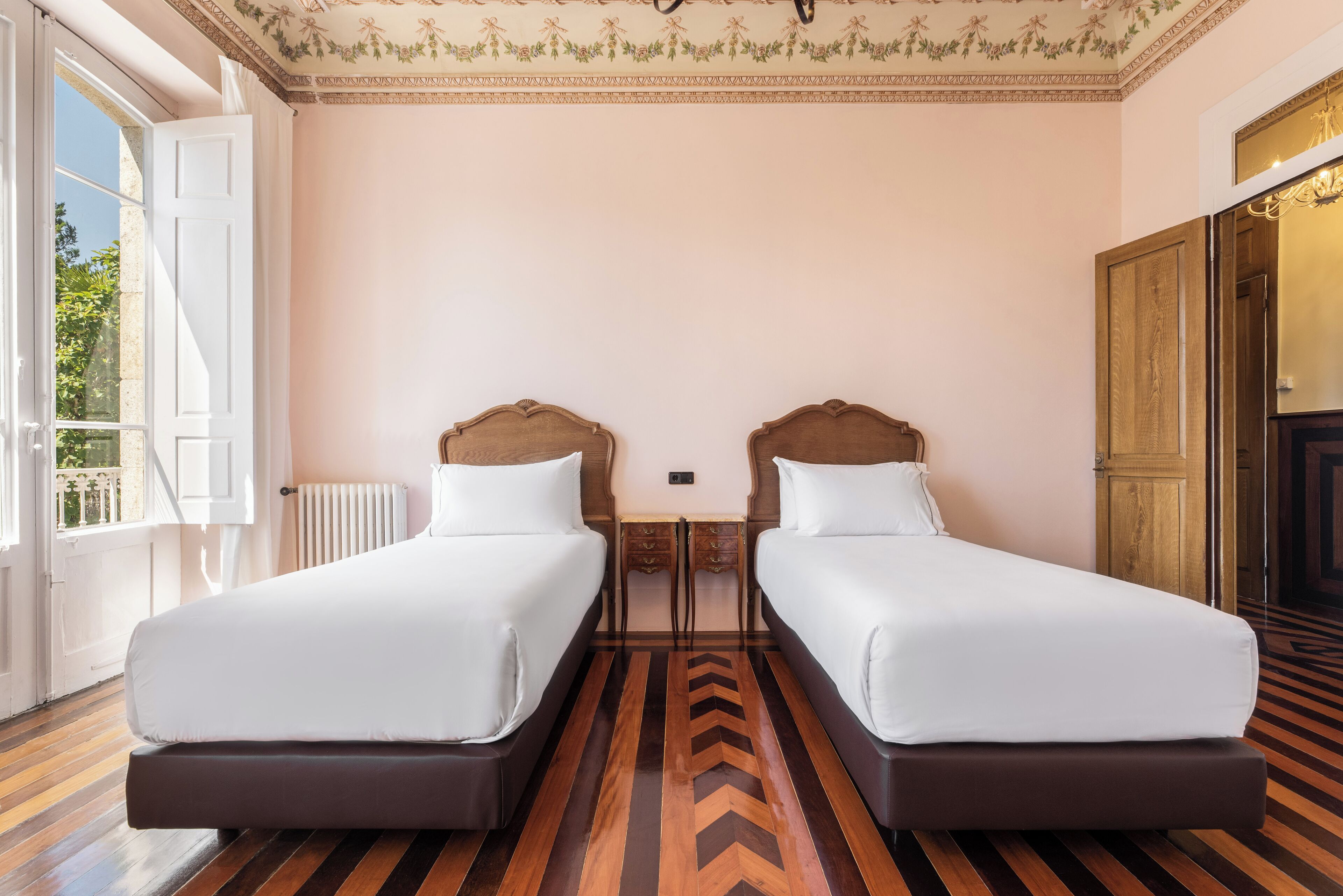 Habitació d'hotel amb dos llits, un sòl de fusta, una taula petita i vistes a l'exterior.
