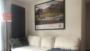 A modern living room with a sofa, a lamp, and a framed landscape painting on the wall. - Stylish annexe in Caernarfon (Caernarfon)