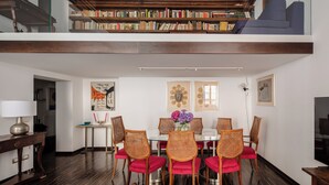 A dining area with a glass table, wicker chairs, and a red cushion. Above the table, there are framed artworks and a bookshelf filled with books. - Elegant apartment in the heart of Rome (Roma)