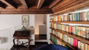 A room with a wooden bookshelf filled with books, a blue chair, and a wooden table with a decorative item. - Elegant apartment in the heart of Rome (Roma)