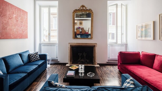 A living room with a blue sofa, a red sofa, a black coffee table, and a fireplace. - Elegant apartment in the heart of Rome (Roma)