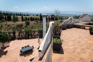 Eine Dachterrasse mit Tisch und Stühlen, Topfpflanzen und Blick auf ferne Berge.