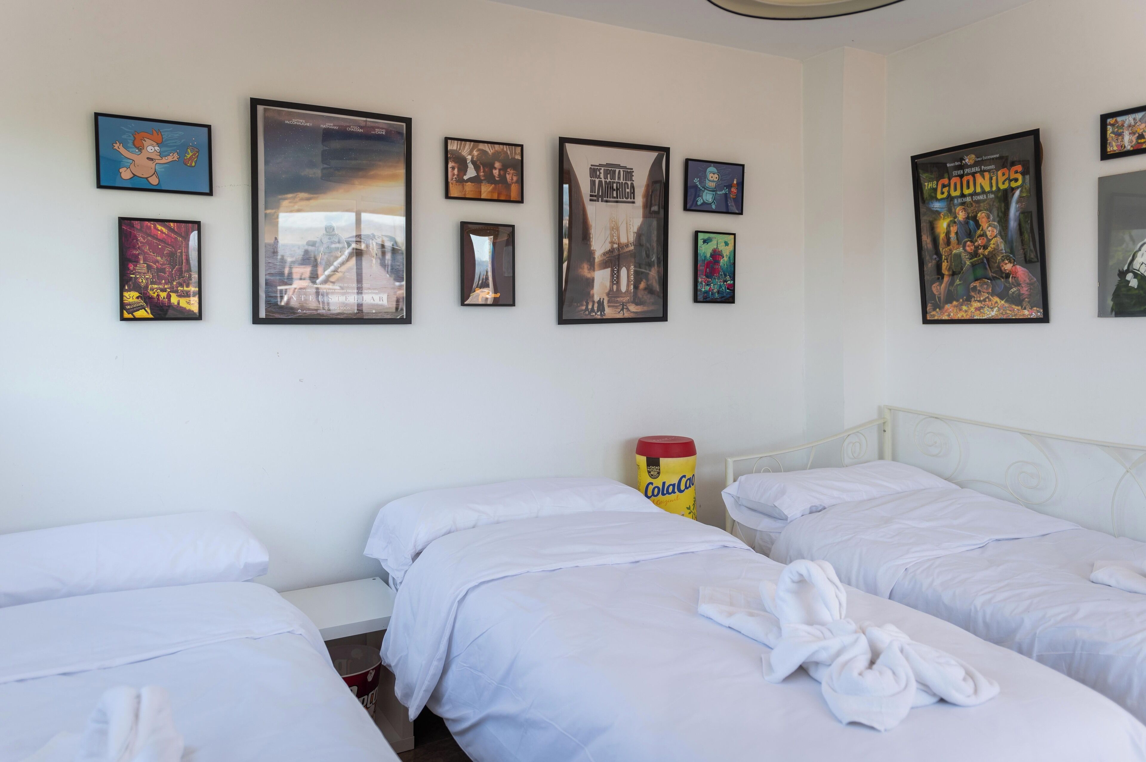 A hotel room with three beds, white bedding, and a wall adorned with various framed posters.