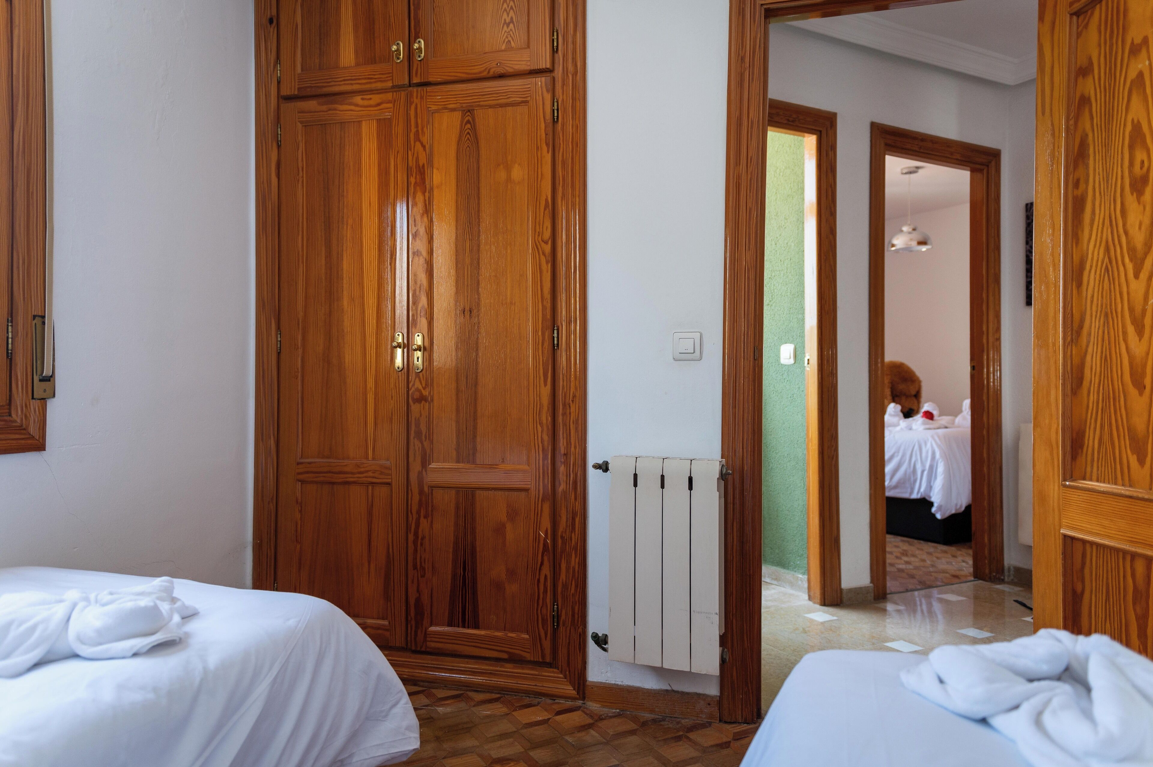 A hotel room with wooden wardrobes, a radiator, and a bed with white bedding.