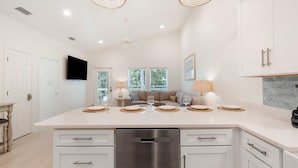 Una cocina moderna con una isla grande, armarios blancos y una zona de comedor con sofá y mesa.